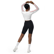 Load image into Gallery viewer, Image of a model from the bac view showcasing the sleeve logo pattern which appears on both sleeves, of the white cropped luxury activewear top designed by Red Valenteen. Model wearing contrasting black bike shorts and white sports shoes to highlight the white fashion piece top design.