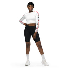Load image into Gallery viewer, image of a women standing face on wearing Red Valenteen luxury, comfort fit and figure hugging white cropped active wear top with bold red and black repeat logo pattern on sides of both sleeves. Model is wearing black bike pants to really accentuate the look and white sports shoes and socks.