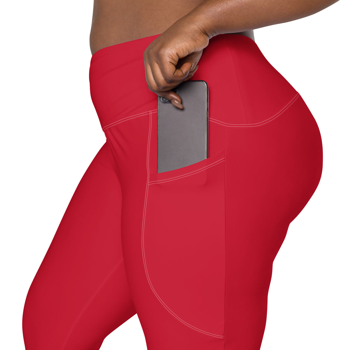 Red high-waisted leggings, with white seam stitching, with a side pocket holding a gray smartphone, shown on a model against a white background.