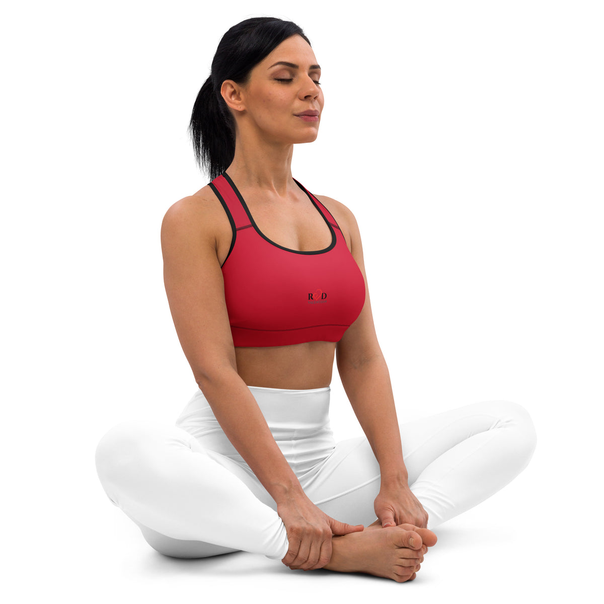 Woman in red sports bra and white pants sitting cross-legged on a white background