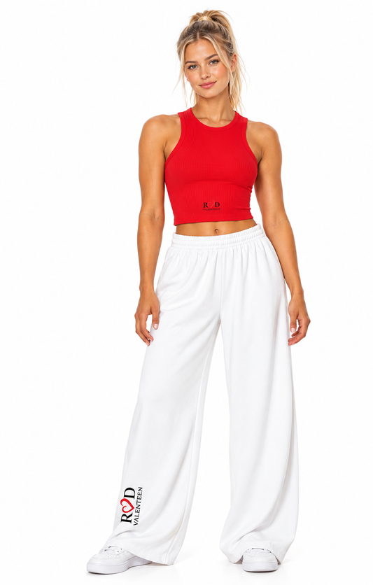 Model wearing red racerback tank top with loose wide leg white pants with the Red Valenteen logo appearing on the base of the right leg, and centre low on the top, on a white background.