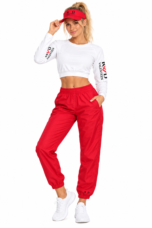 A woman modeling a matching activewear set consisting of a white long-sleeve crop top with red and black 'Red Valenteen' sleeve graphics, bright red jogger sweatpants, a red visor, and white sneakers, against a plain white background.