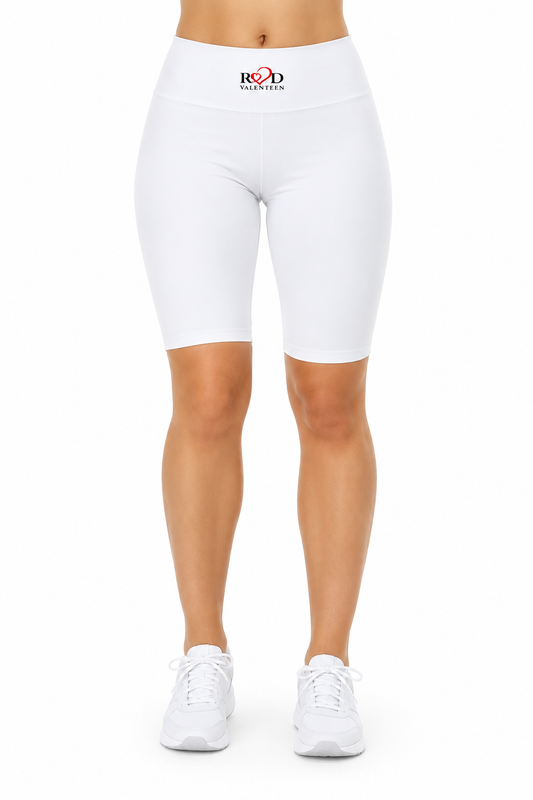 White high-waisted biker shorts with a small red and black logo on the front waistband, shown on a model from the waist down wearing white sneakers against a plain white background.
