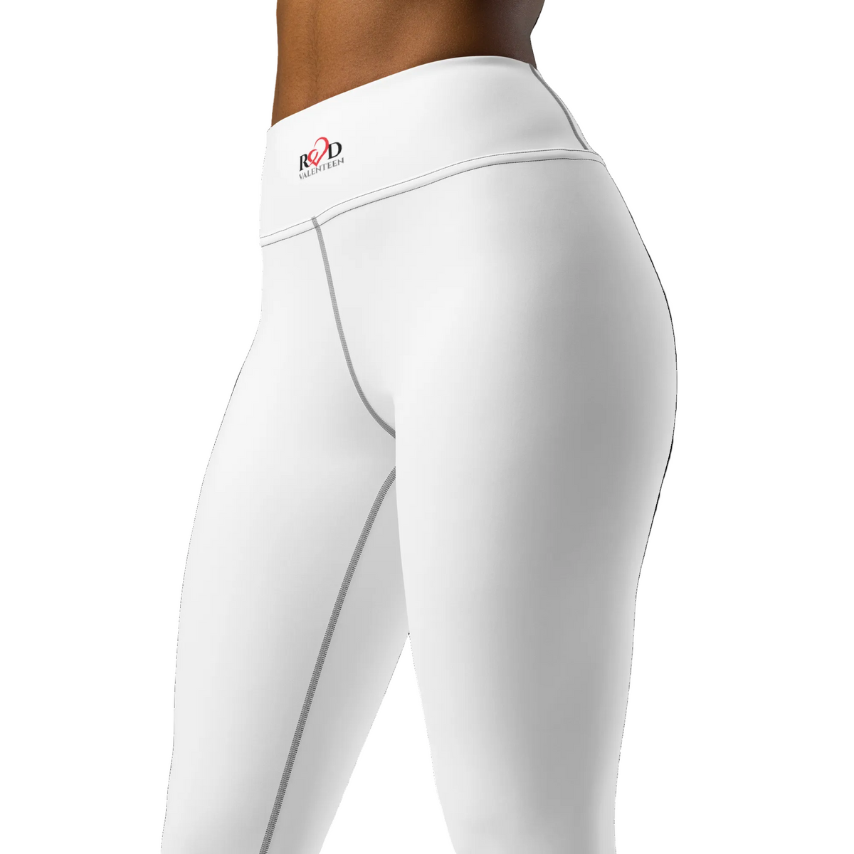 Left front close up of model wearing white leggings with contrast stitch on seams and small Red Valenteen logo on waistband, on white background. 