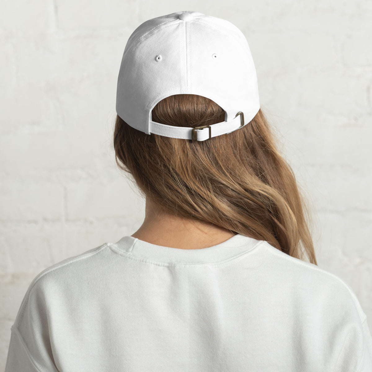 Back view of a white cap on the head of  model, wearing a white tshirt and a white wall behind them.