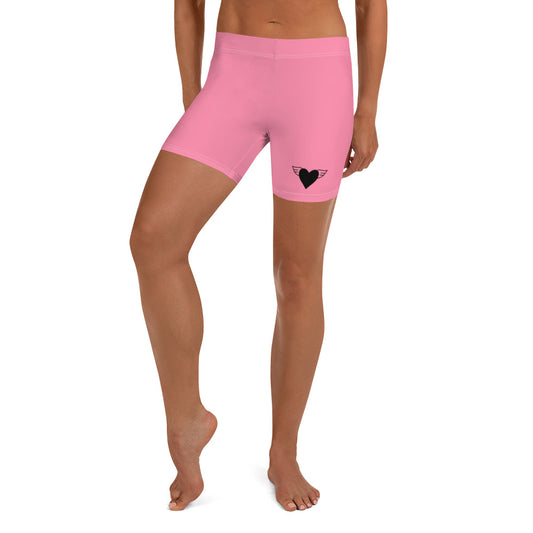 A pair of pink sport activewear shorts with a heart applique on the front, standing mid-calf in length.