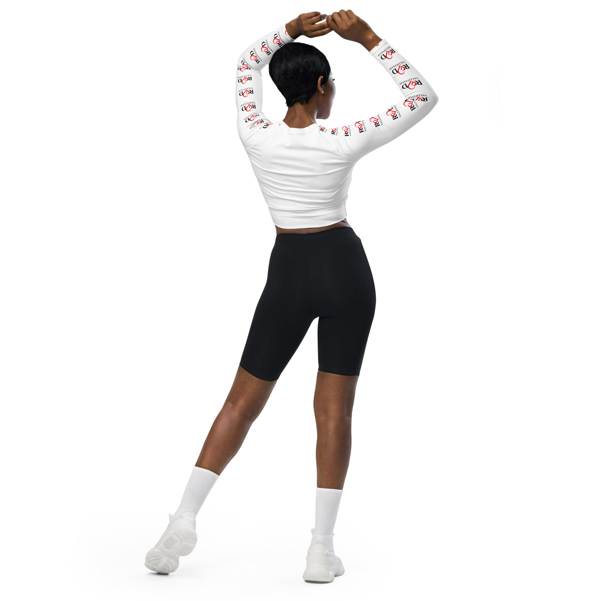 A model from behind wearing a white long-sleeve crop top with red and black logo Red Valenteen graphic prints down the sleeves, paired with black biker shorts, white socks, and white sneakers, set against a solid white background.
