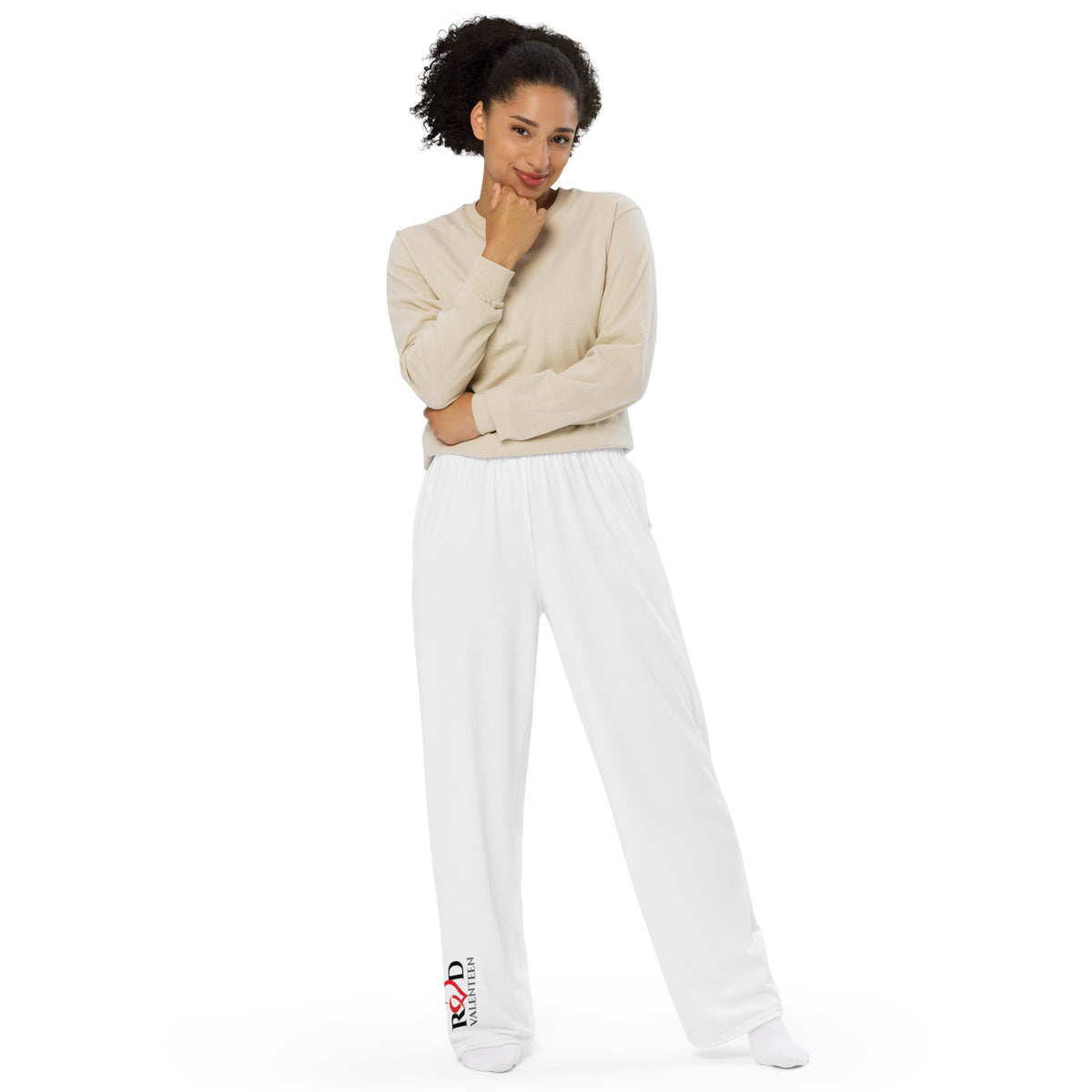 Woman wearing a beige sweater and white pants with 'Red Valenteen' logo on a white background